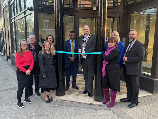 group photo outside a building with dark pillows, teal ribbon being cut