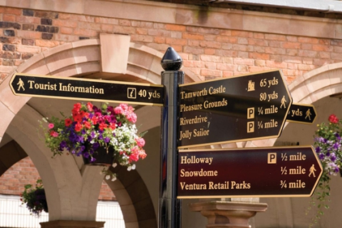 A signage post with hanging baskets of flowers behind it
