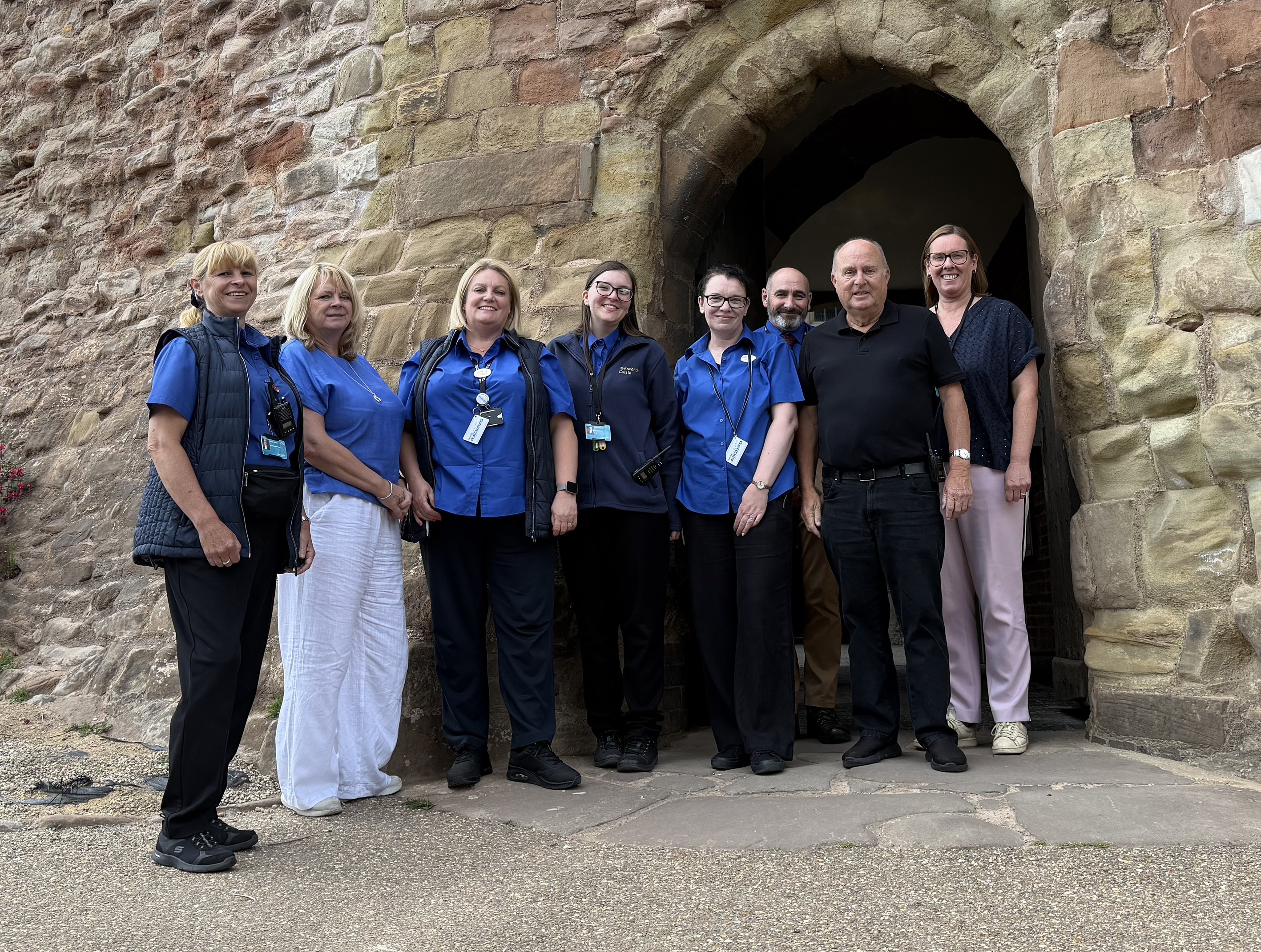 group of people standing outside a brick archway wearing blue top uniform