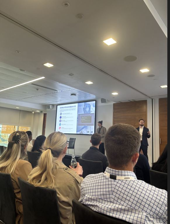 photo of people sitting in a room with a person standing upfront by a screen 