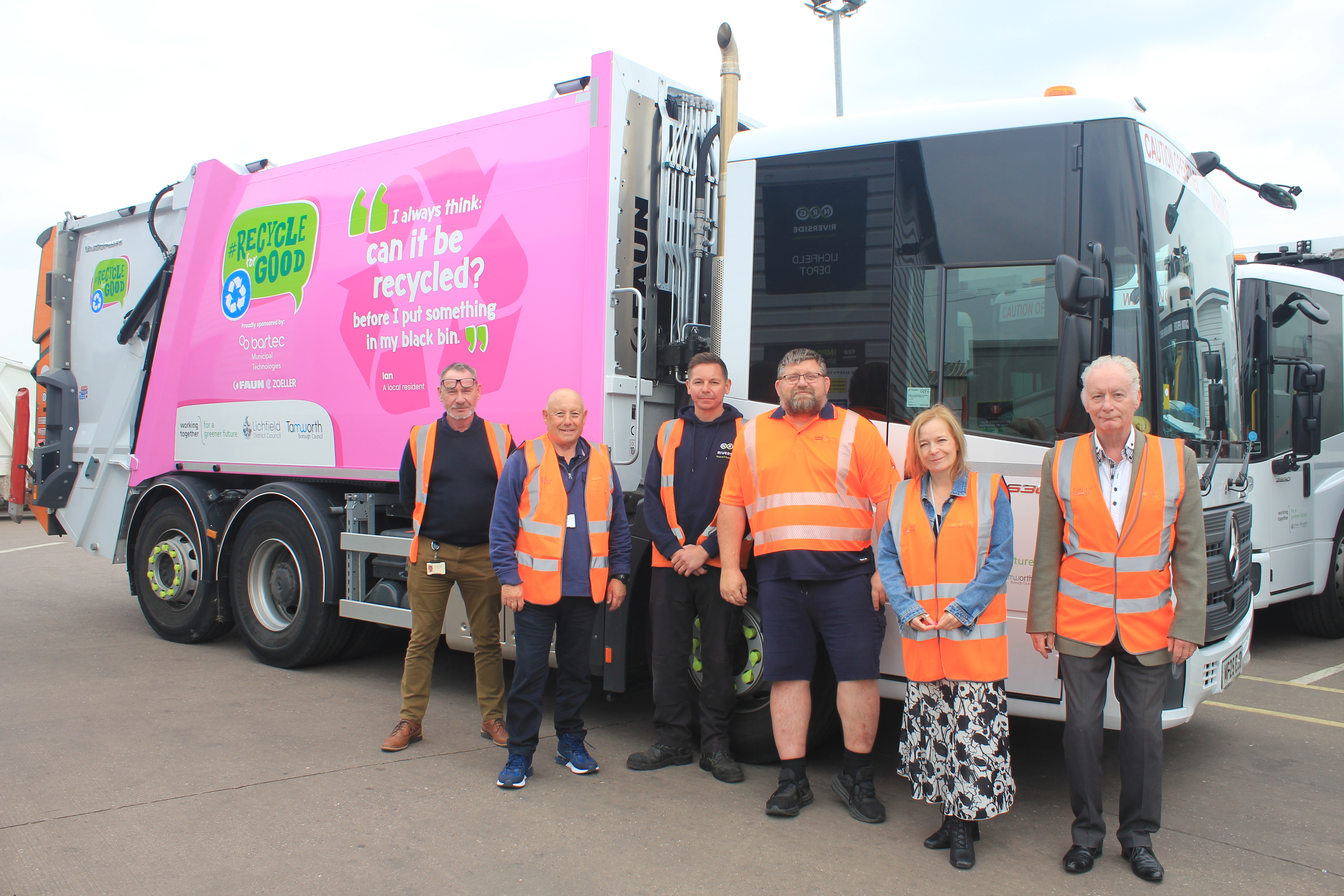 photo of a bin truck with a pink banner and 6 people in orange hi vis jackets