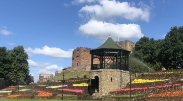 photo of the Castle Grounds with the bandstand and castle in background, blue sky and white clouds plus red, orange and yellow flowers