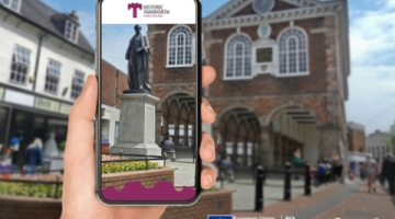 A mobile phone in front of the town hall showing the reality trail app