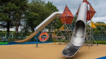 A playground with climbing frame and two metal slides