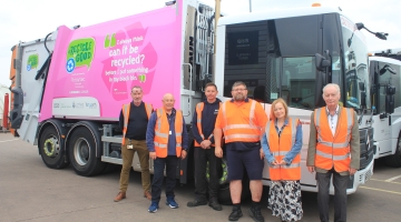 photo of a bin truck with a pink banner and 6 people in orange hi vis jackets